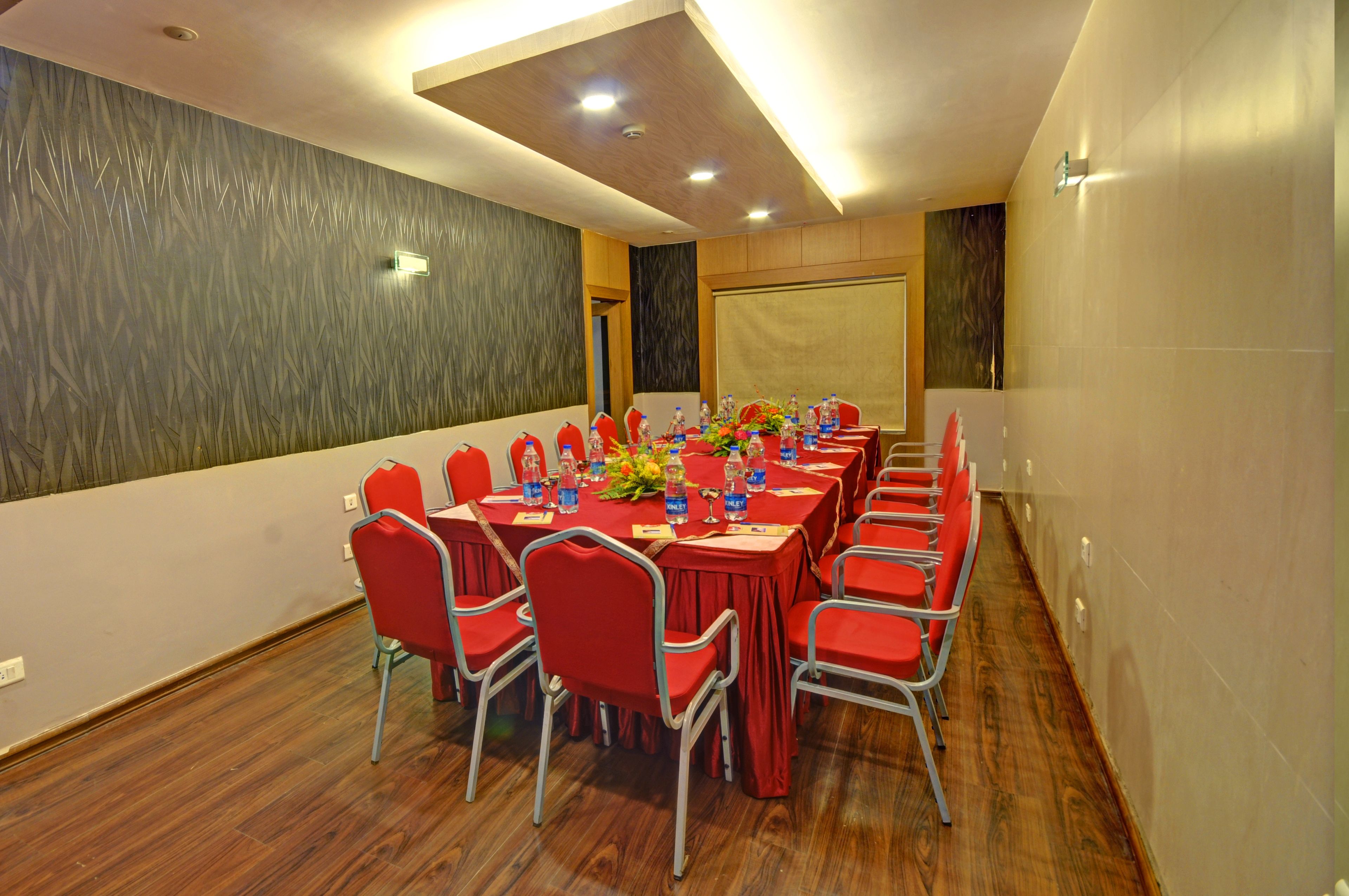 A conference room with a long table, red chairs, and a projector screen.