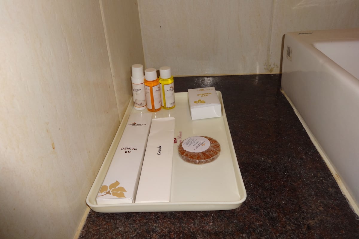 A bathroom with a white countertop holding a dental kit, a shower cap, and three bottles of shampoo.
