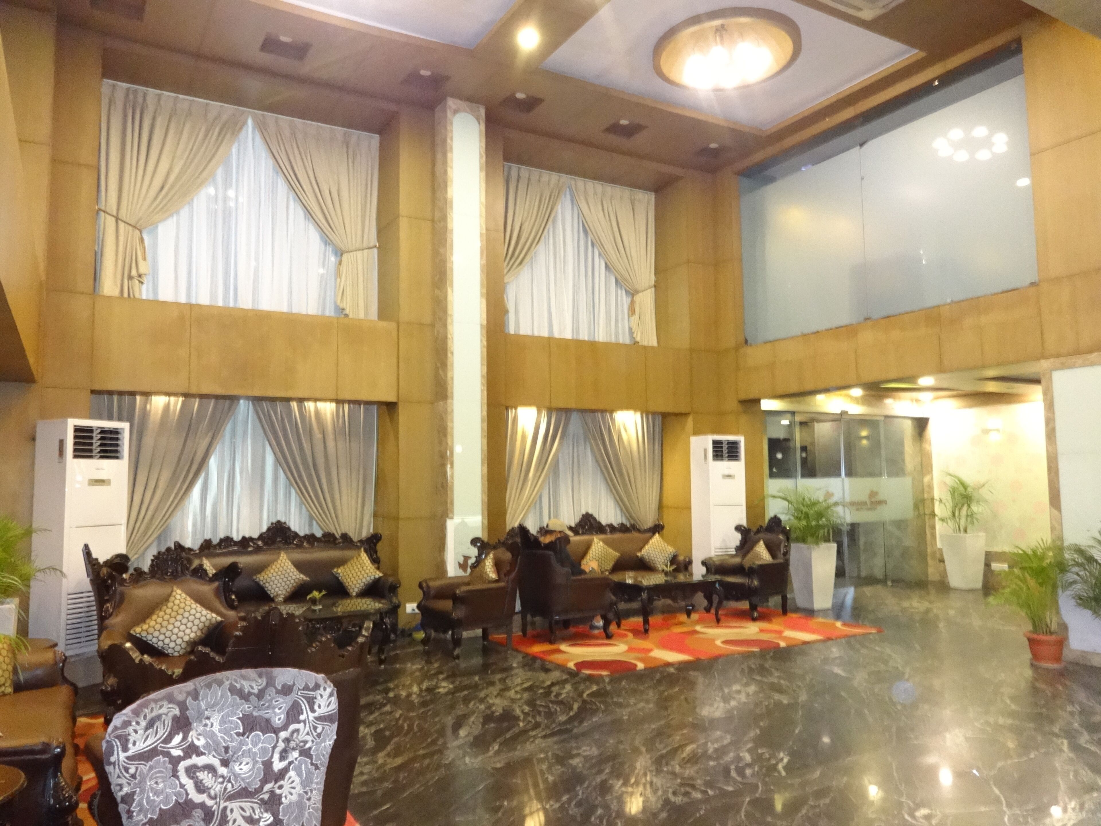 Een ruime lobby met hoge plafonds, grote ramen voorzien van gordijnen, en een centraal zithoek met banken en fauteuils.