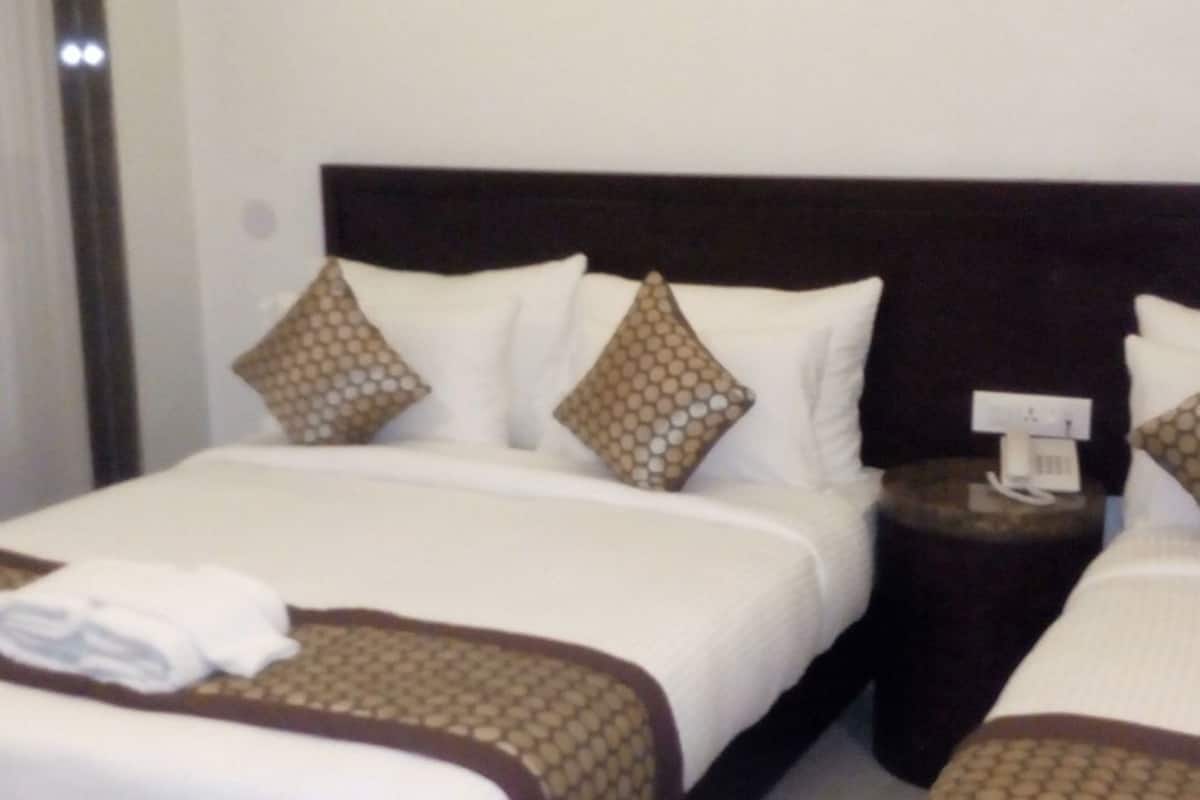 A hotel room with two beds, a bedside table with a phone, and a wall-mounted light.