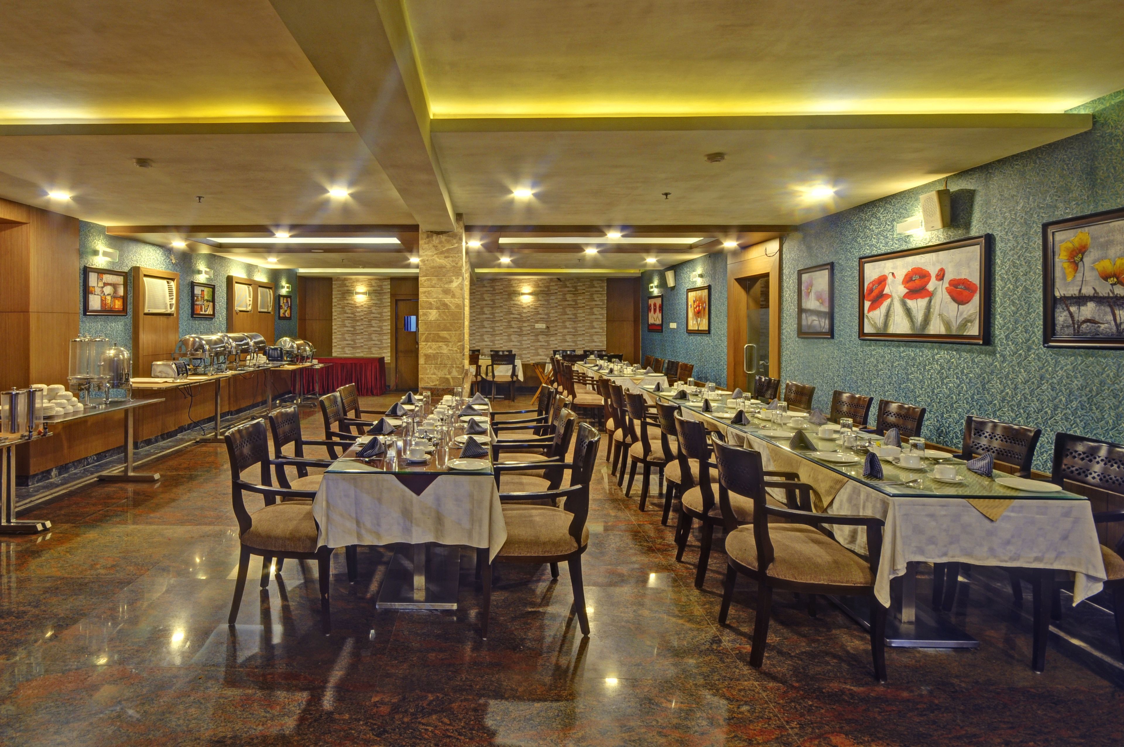 Un comedor amplio con mesas y sillas múltiples, una barra de buffet a la izquierda y obras de arte en las paredes.