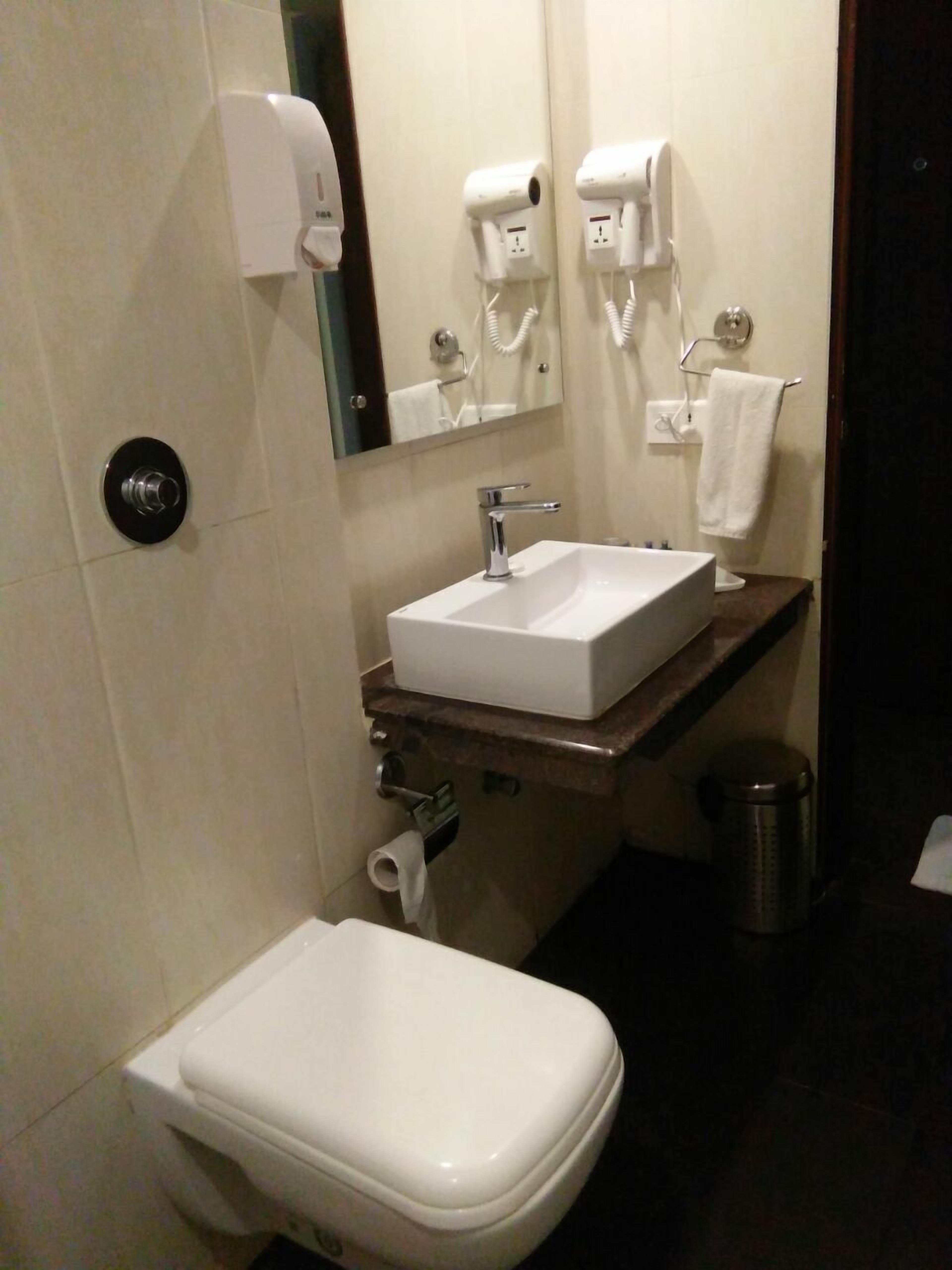 Kylpyhuoneessa on valkoinen wc-istuin, peilillä varustettu pesuallas ja kaksi käsienkuivaajaa.