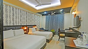 Quarto de hotel com duas camas, uma escrivaninha, uma cadeira, toucador com espelho e ventoinha de teto.