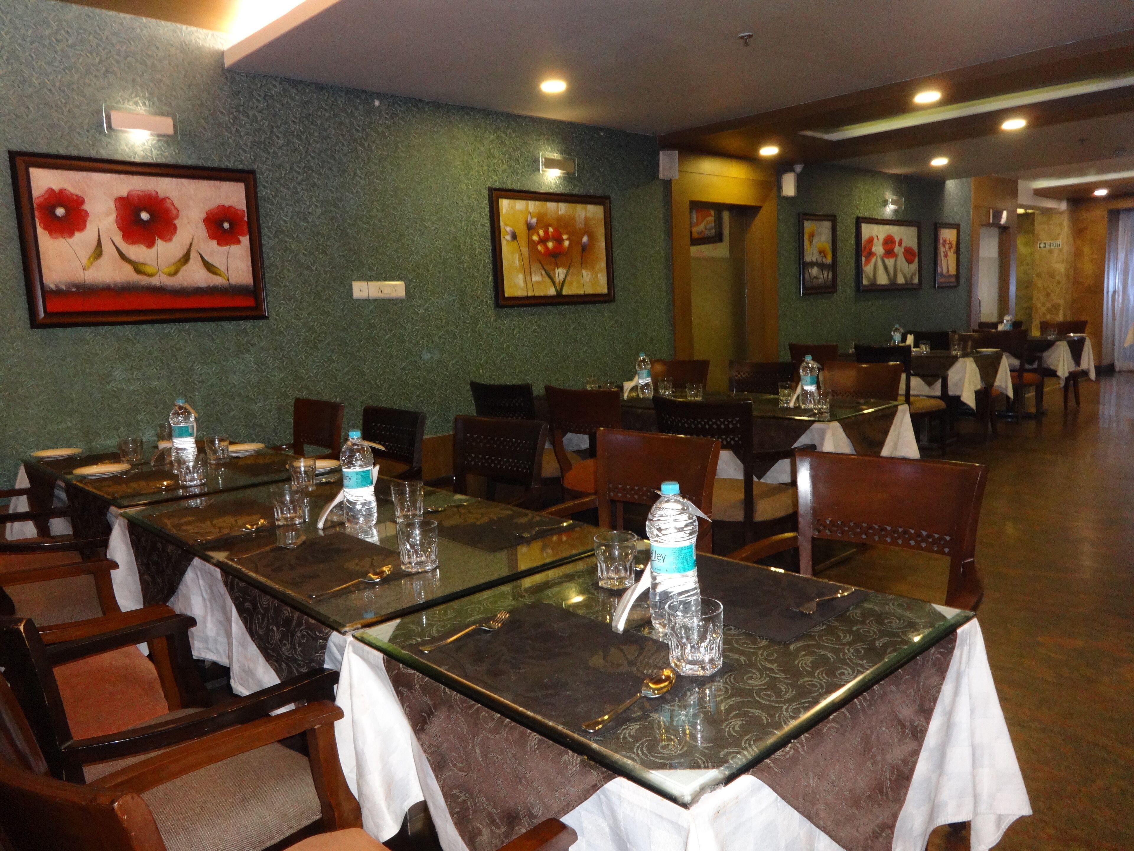 A restaurant with glass tables and chairs, water bottles, and framed floral artwork on the walls.