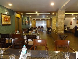 Un restaurante con varias mesas y sillas, botellas de agua sobre las mesas y obras de arte enmarcadas en las paredes.