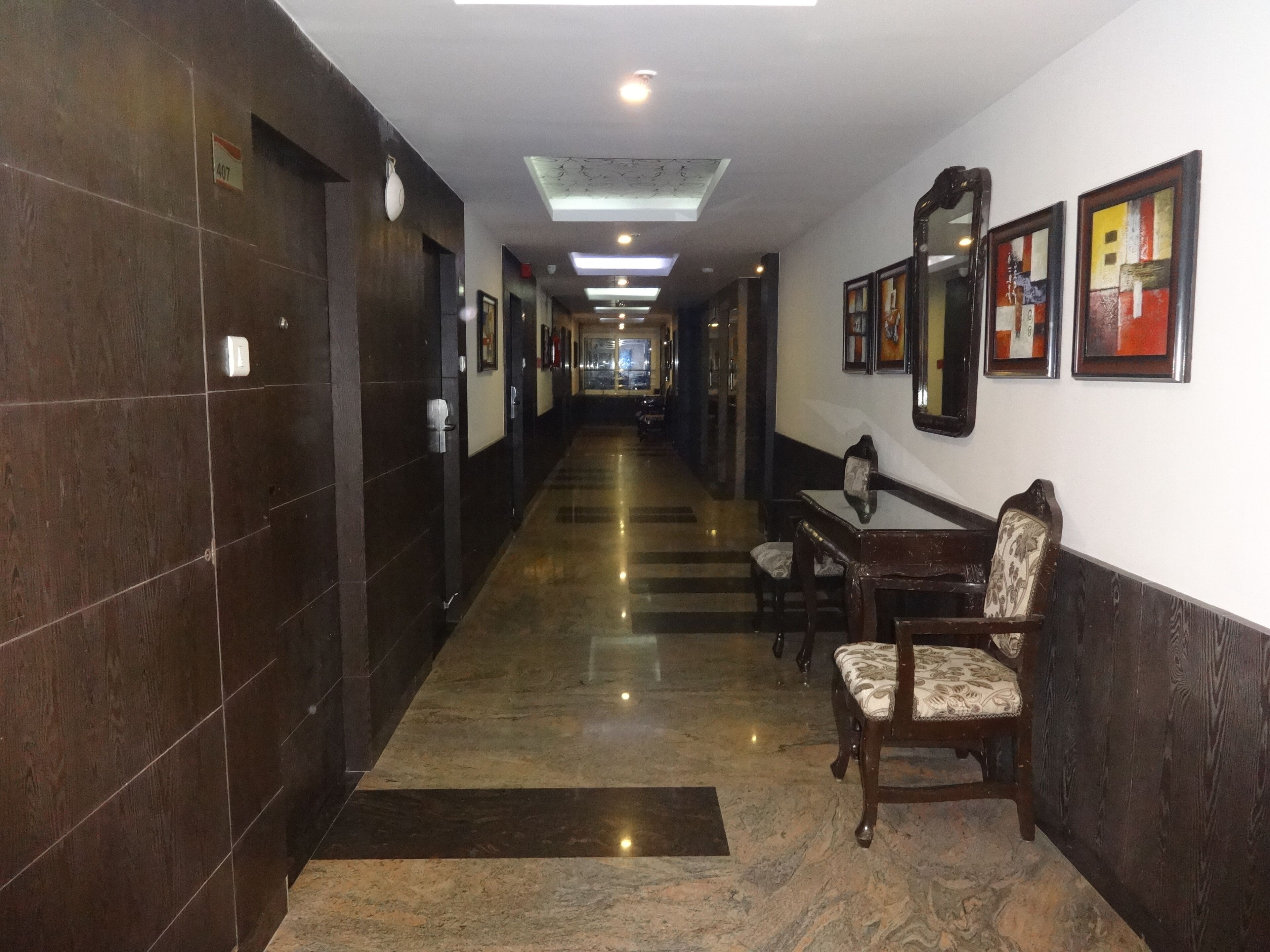 A hotel corridor with dark wooden walls, a marble floor, and a dining area with wooden furniture.