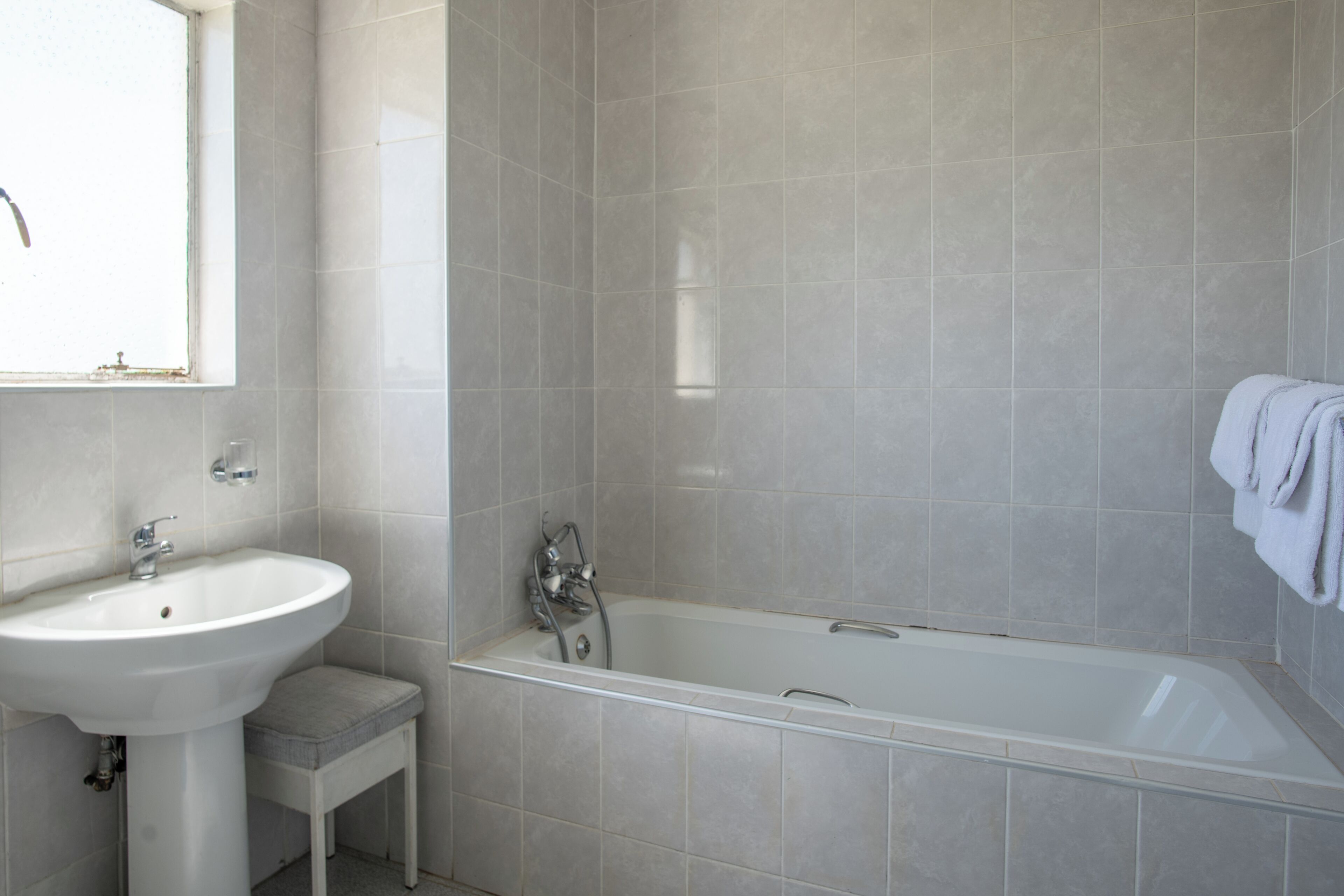 Un baño con un lavamanos blanco, una bañera y un taburete pequeño.
