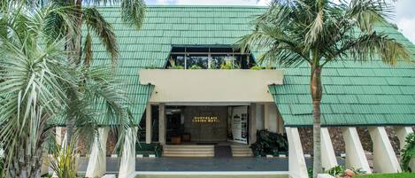 A hotel entrance with a green roof, palm trees, and a water feature in front.