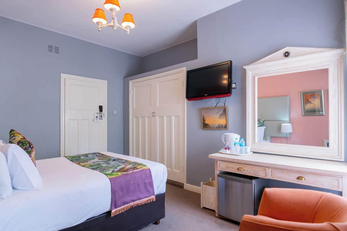A hotel room with a bed, a desk with a mirror, a television, and a door.