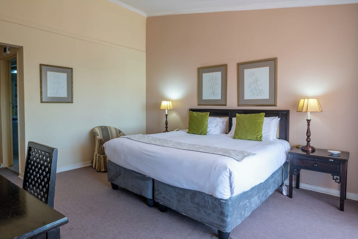 A neatly arranged bedroom with a large bed, two bedside lamps, and a chair.