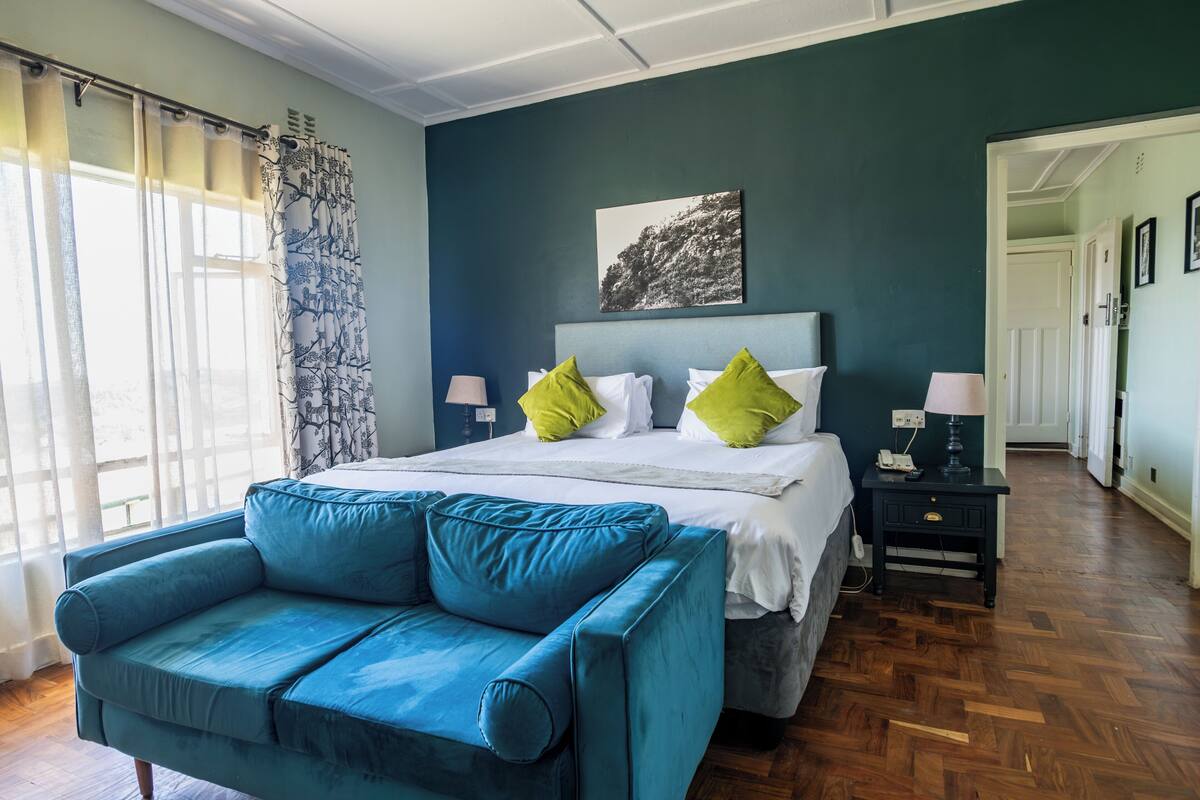 A bedroom with a bed, a blue sofa, a nightstand, and a painting on the wall.