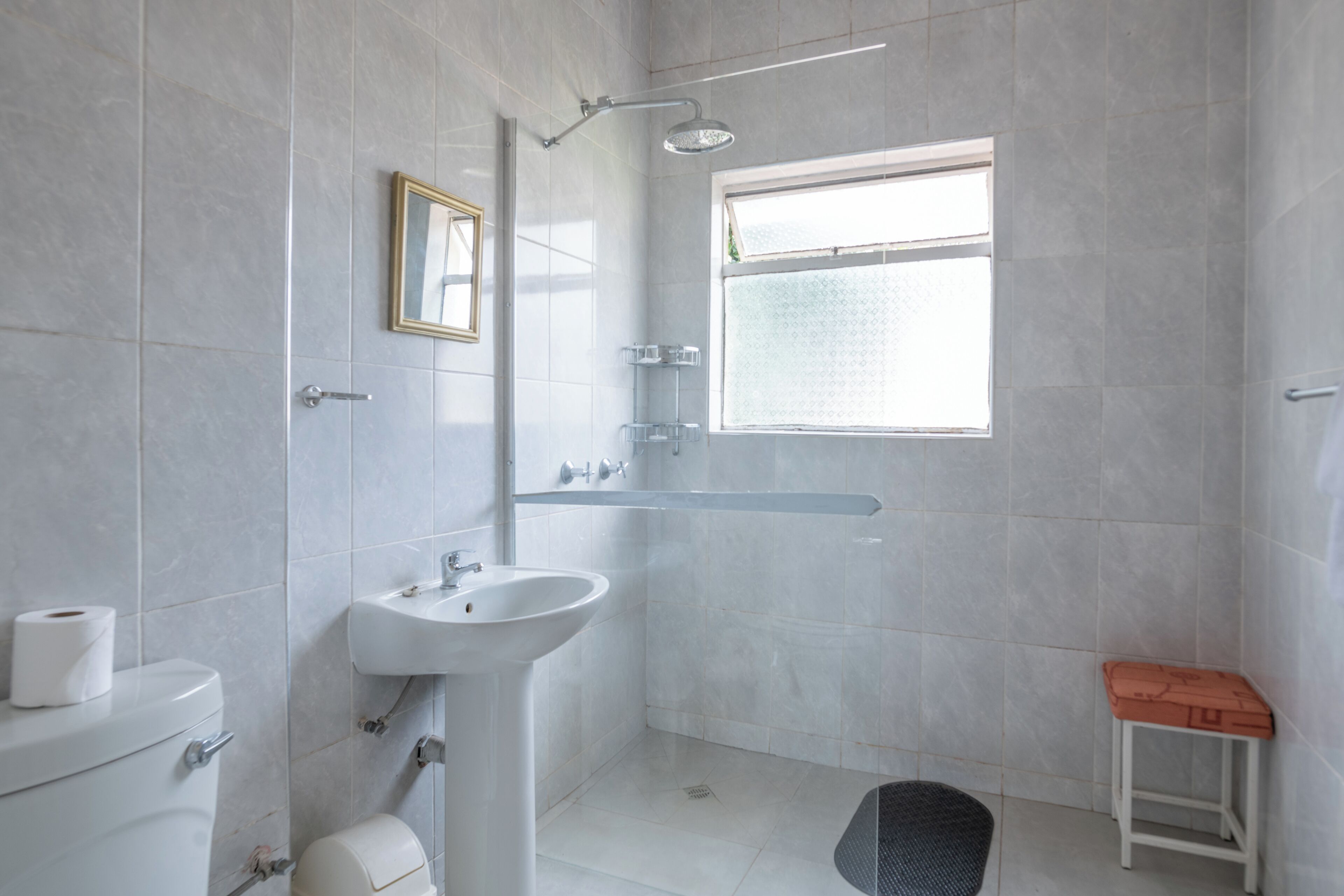 A modern bathroom with a toilet, sink, shower, and a small stool.