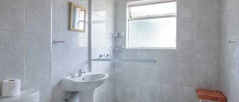 A modern bathroom with a toilet, sink, shower, and a small stool.