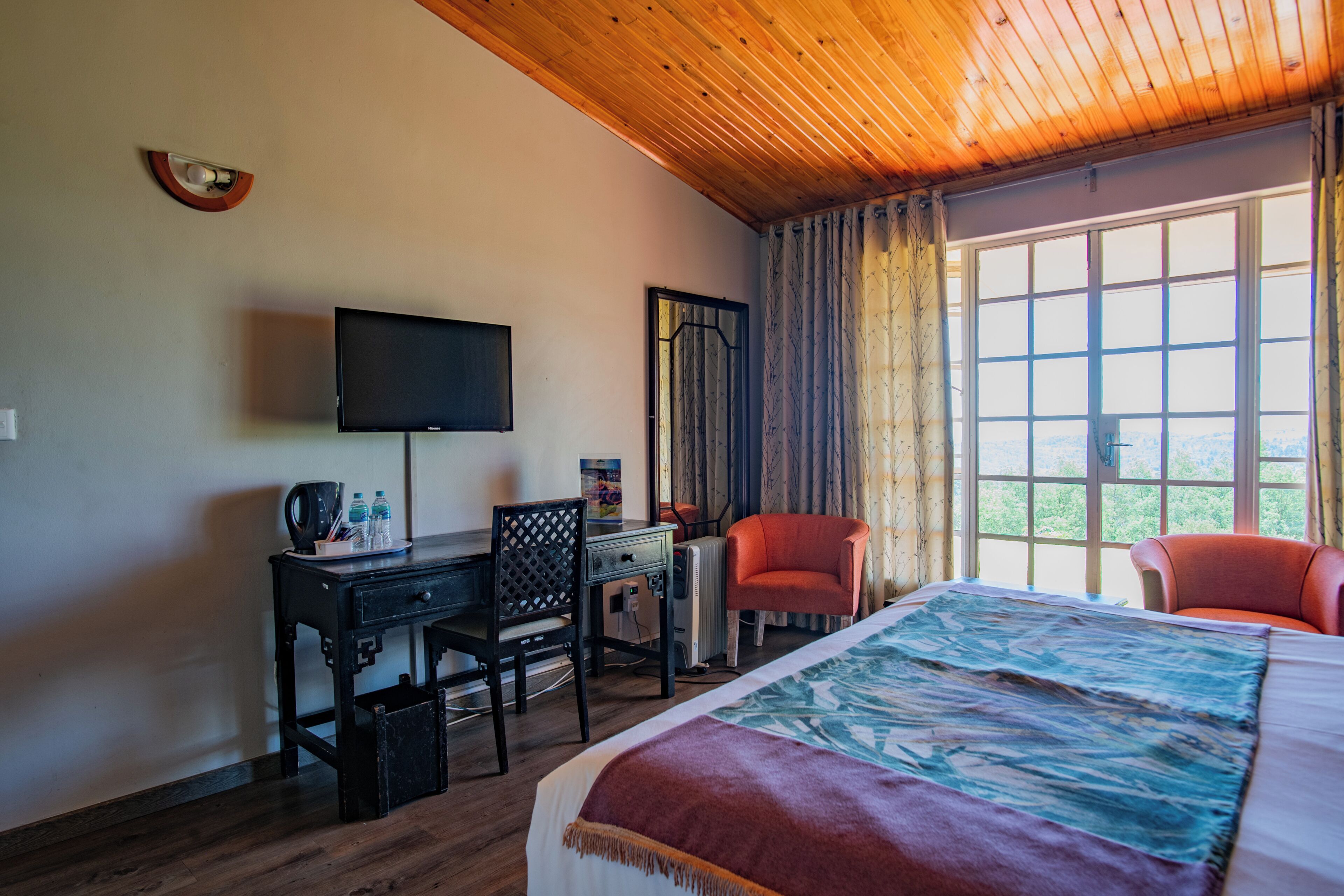 Habitación de hotel con cama, escritorio con silla, televisor y ventana con cortinas.