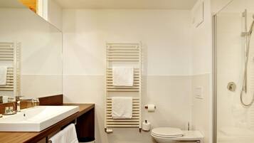 Un baño moderno con tocador de madera, inodoro, ducha y un espejo grande.