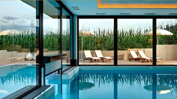 Une piscine intérieure moderne avec des parois en verre transparent, des chaises longues et des parasols.