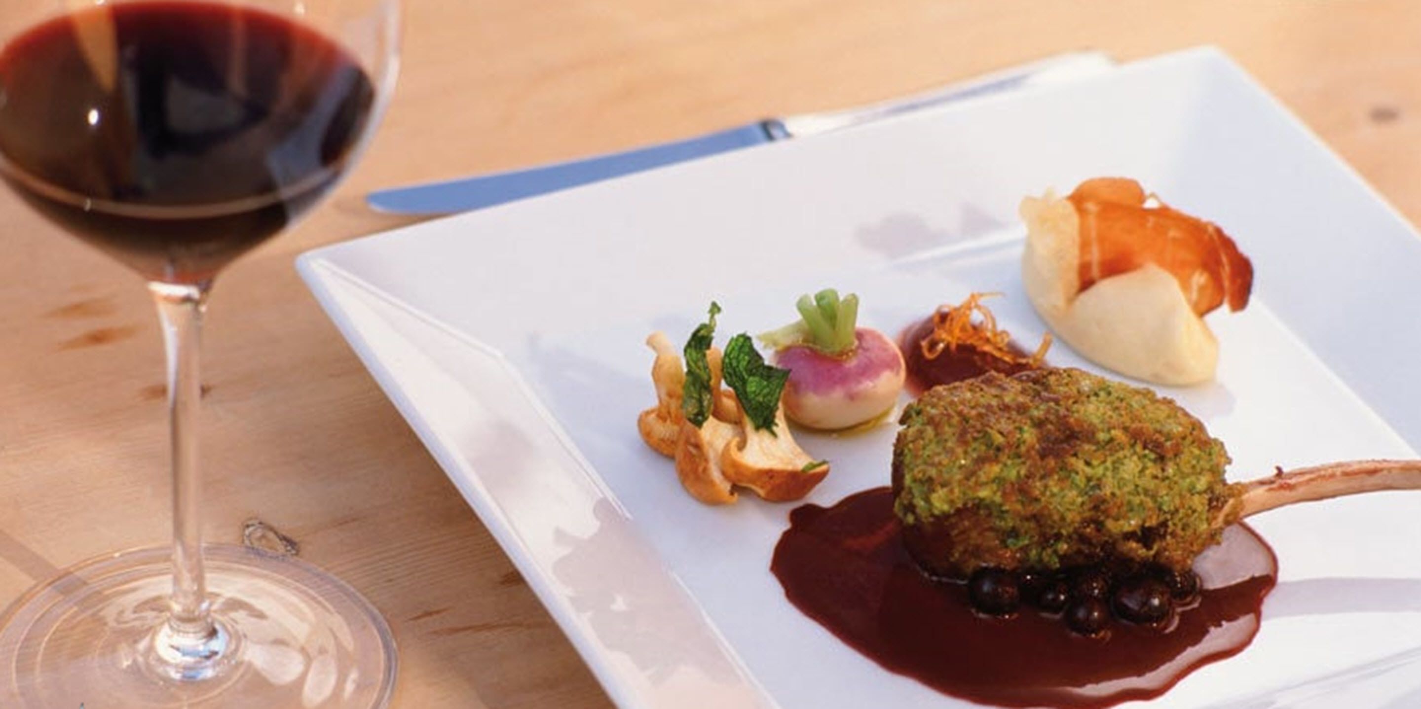A white plate with a variety of food items, including a meat dish, a vegetable, and a dessert, accompanied by a glass of red wine.