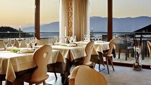 Un espace repas avec des tables dressées pour le repas, de grandes fenêtres offrant une vue sur les montagnes et un balcon doté d’une balustrade.