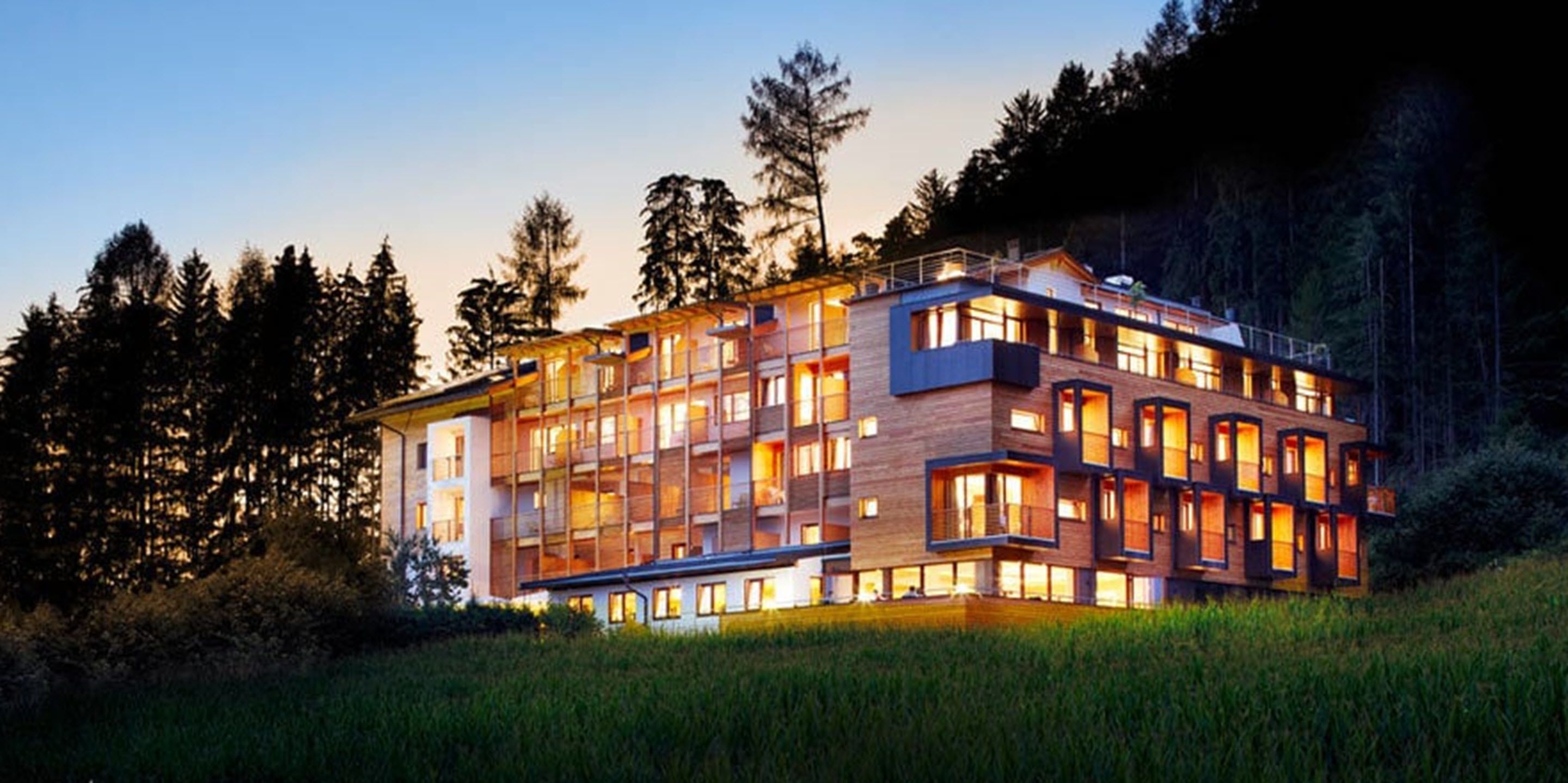 Un hôtel à plusieurs étages, doté d’un design moderne, de balcons et de grandes fenêtres, et situé dans une zone boisée.