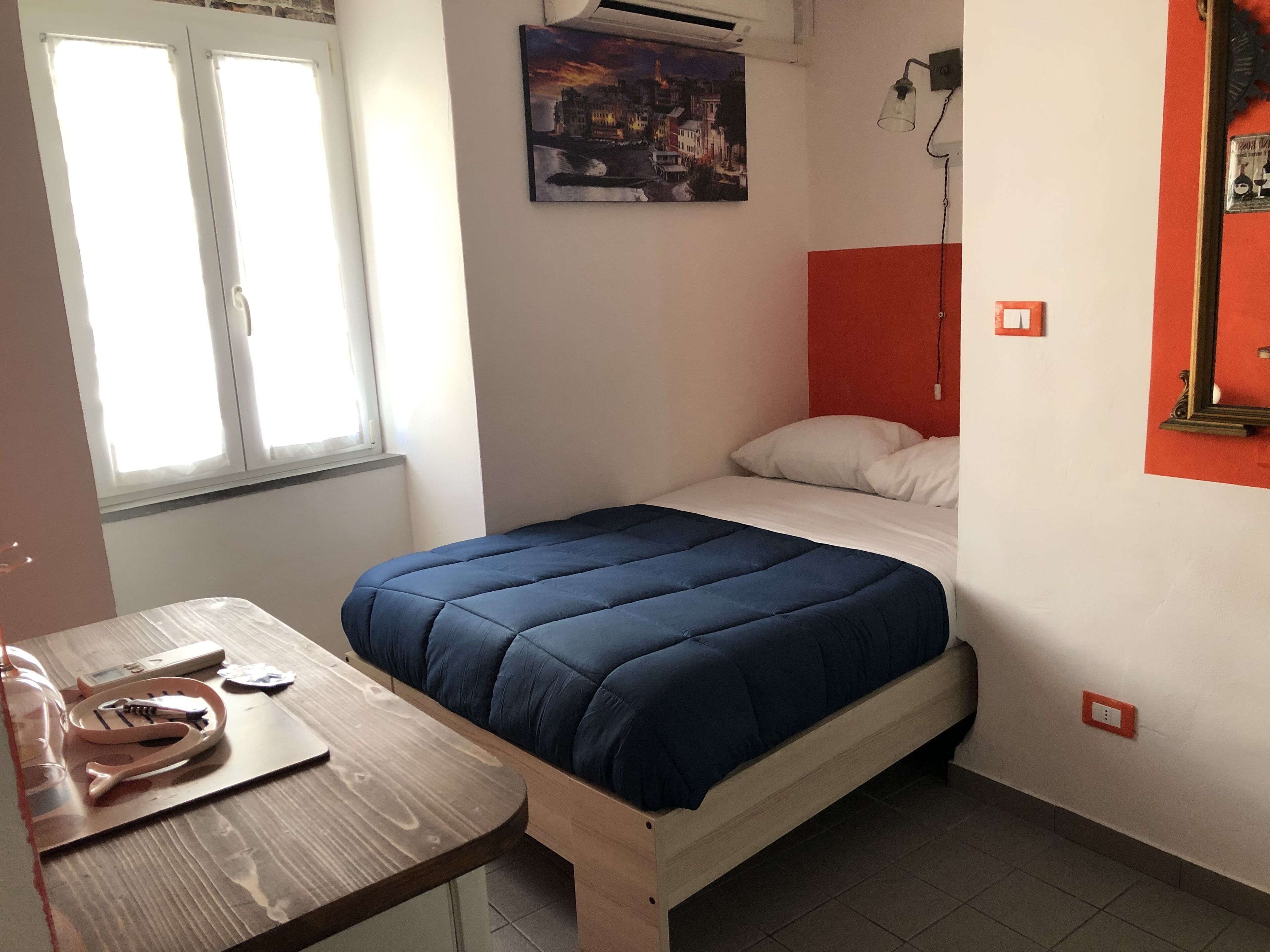 A bedroom with a bed, a wooden desk, a window, and a painting on the wall.
