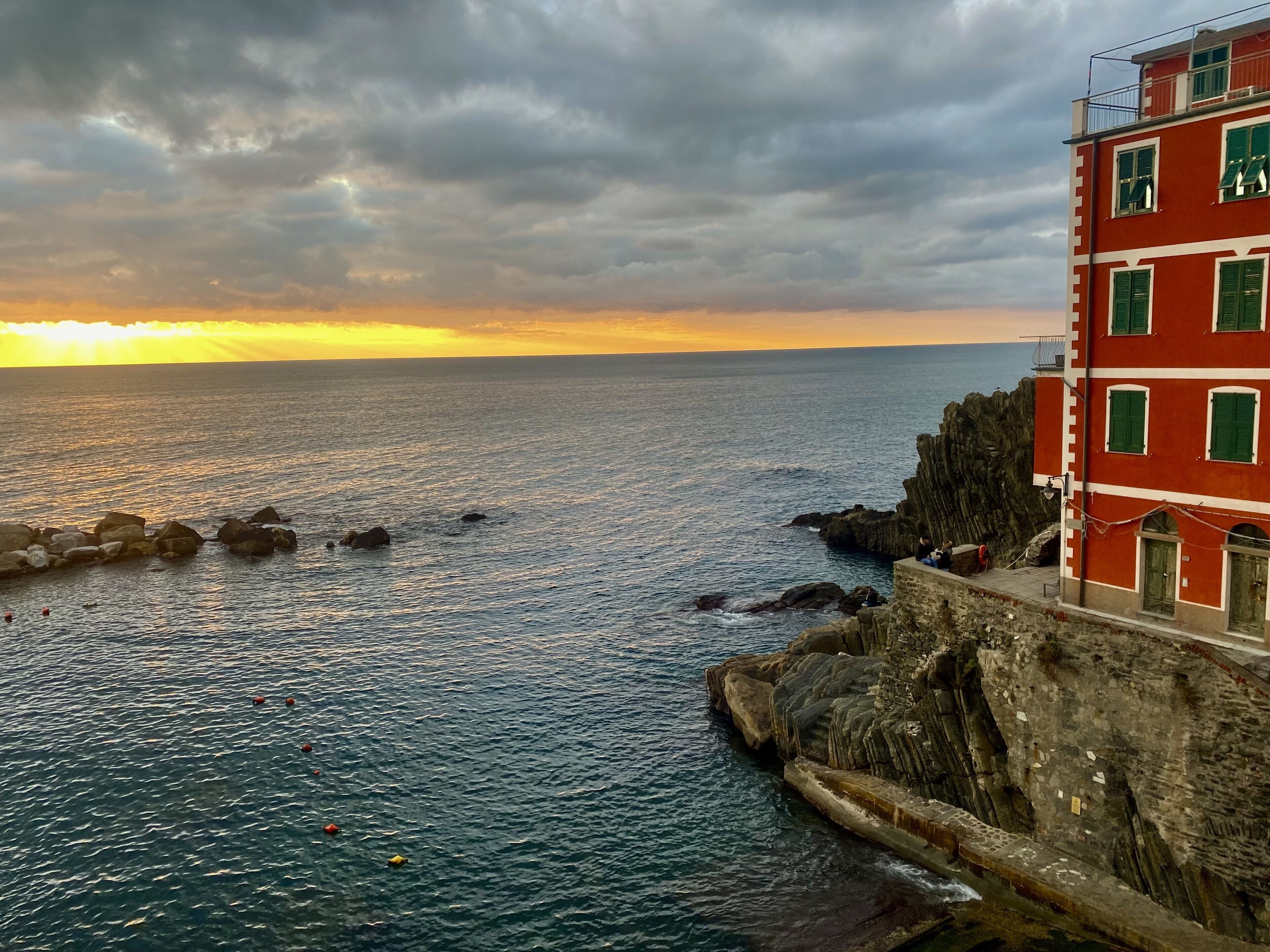 Un edificio costero con fachada de piedra y detalles en rojo y blanco, con vistas al mar.