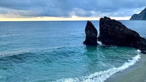 Escena costera con dos formaciones rocosas destacadas en el agua, una playa arenosa y un cielo nublado.