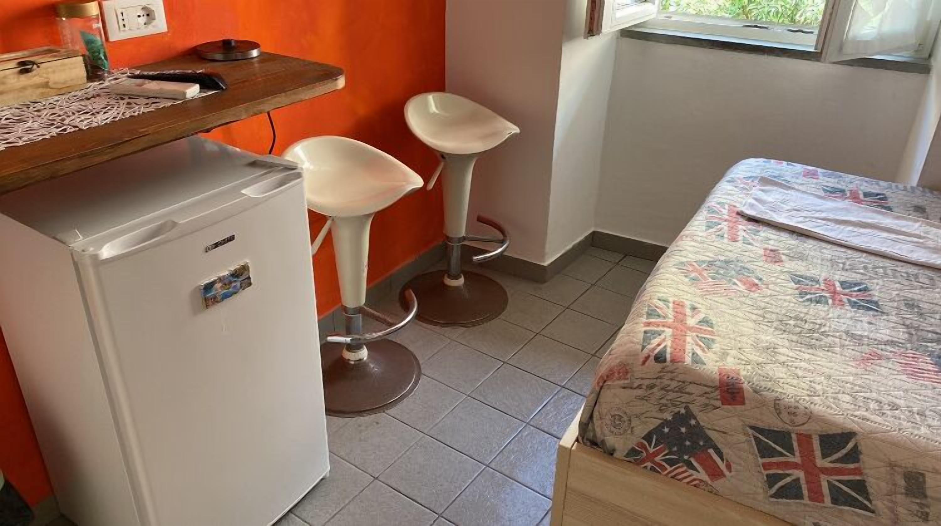 Une petite cuisine équipée d’un réfrigérateur, de deux tabourets de bar et d’un lit recouvert d’une courtepointe ornée de motifs de drapeaux.