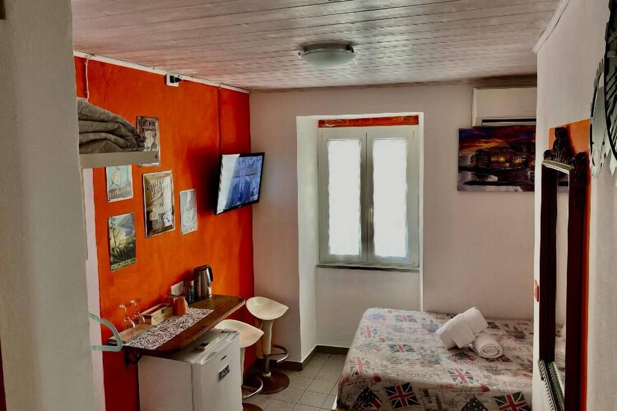 A small, compact room with a bed, a desk, and a chair. There is a window with a view of the outside.