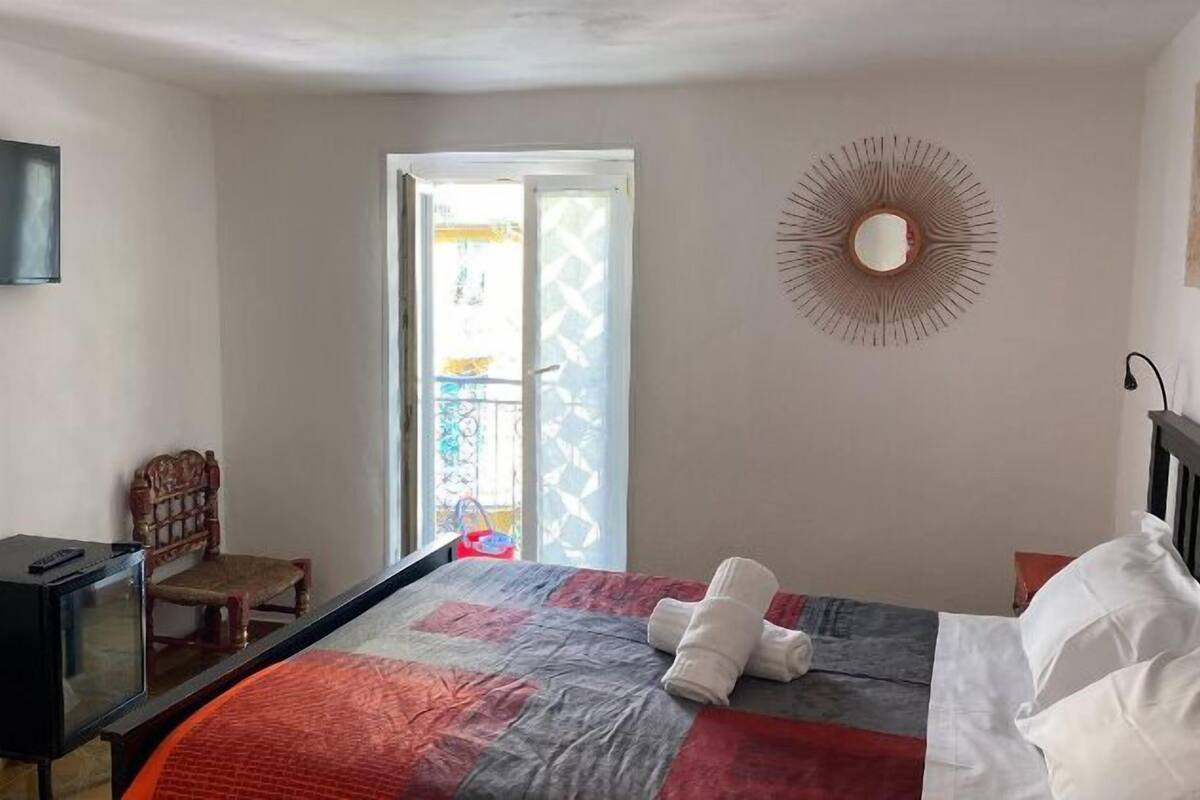 A bedroom with a bed, a chair, a TV, and a window.