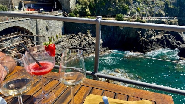 Una mesa de madera con copas de vino y un plato de comida, con vistas a un río pedregoso.