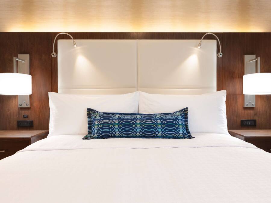 A hotel room with a large bed, two bedside tables, and a headboard with integrated lighting.