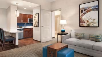Una habitación de hotel moderna con kitchenette, un sofá, una mesita de café y un cuadro de un puente.