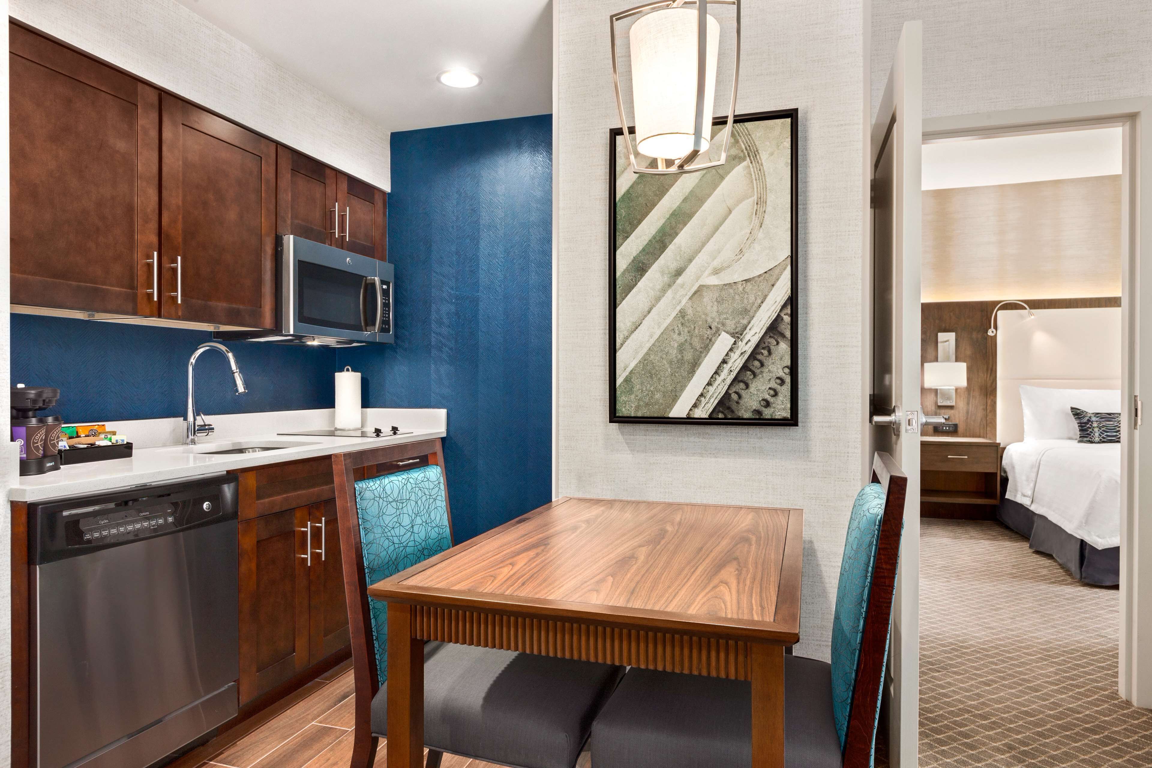 A compact hotel room with a kitchenette, a dining area, and a bed.