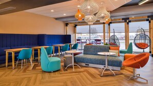 A modern lounge area with blue seating, wooden tables, and unique hanging chairs. - Tru by Hilton Stuttgart, AR (Stuttgart)