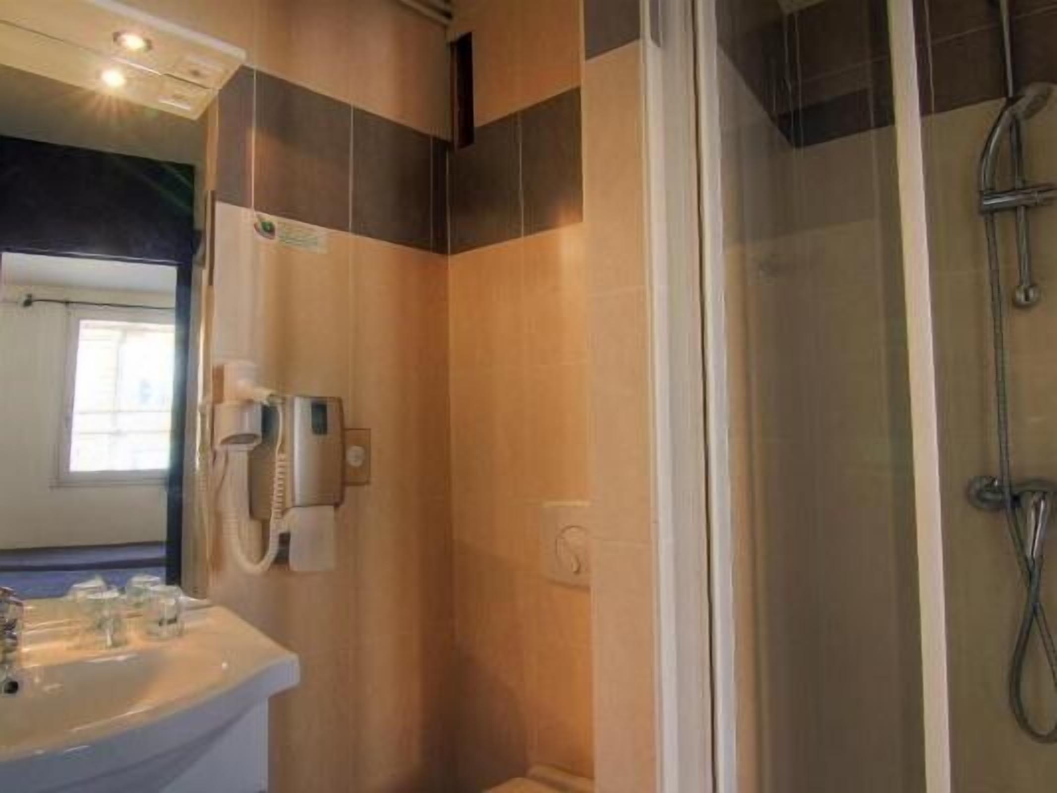 Un baño con lavabo, espejo, ducha con puerta de cristal y teléfono fijo en la pared.