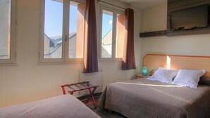 Habitación de hotel con dos camas, una ventana con cortinas, una mesita y un televisor montado en la pared.