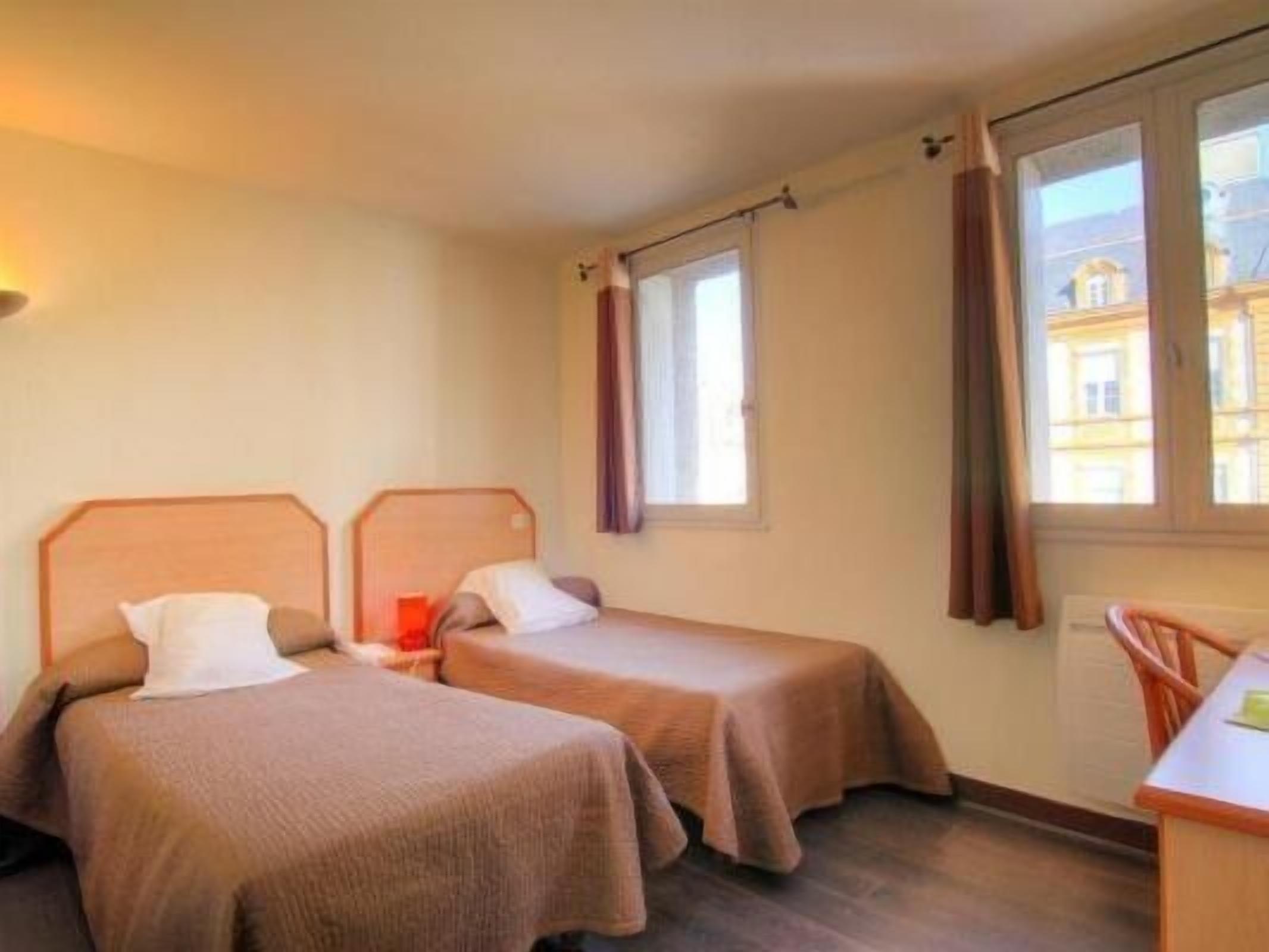 A hotel room with two single beds, a small desk, and a window with curtains.