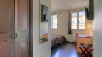 A compact hotel room with a bed, a small desk, a chair, and a television.