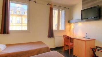 Een hotelkamer met twee bedden, een bureau, een stoel, een televisie en een raam met gordijnen.