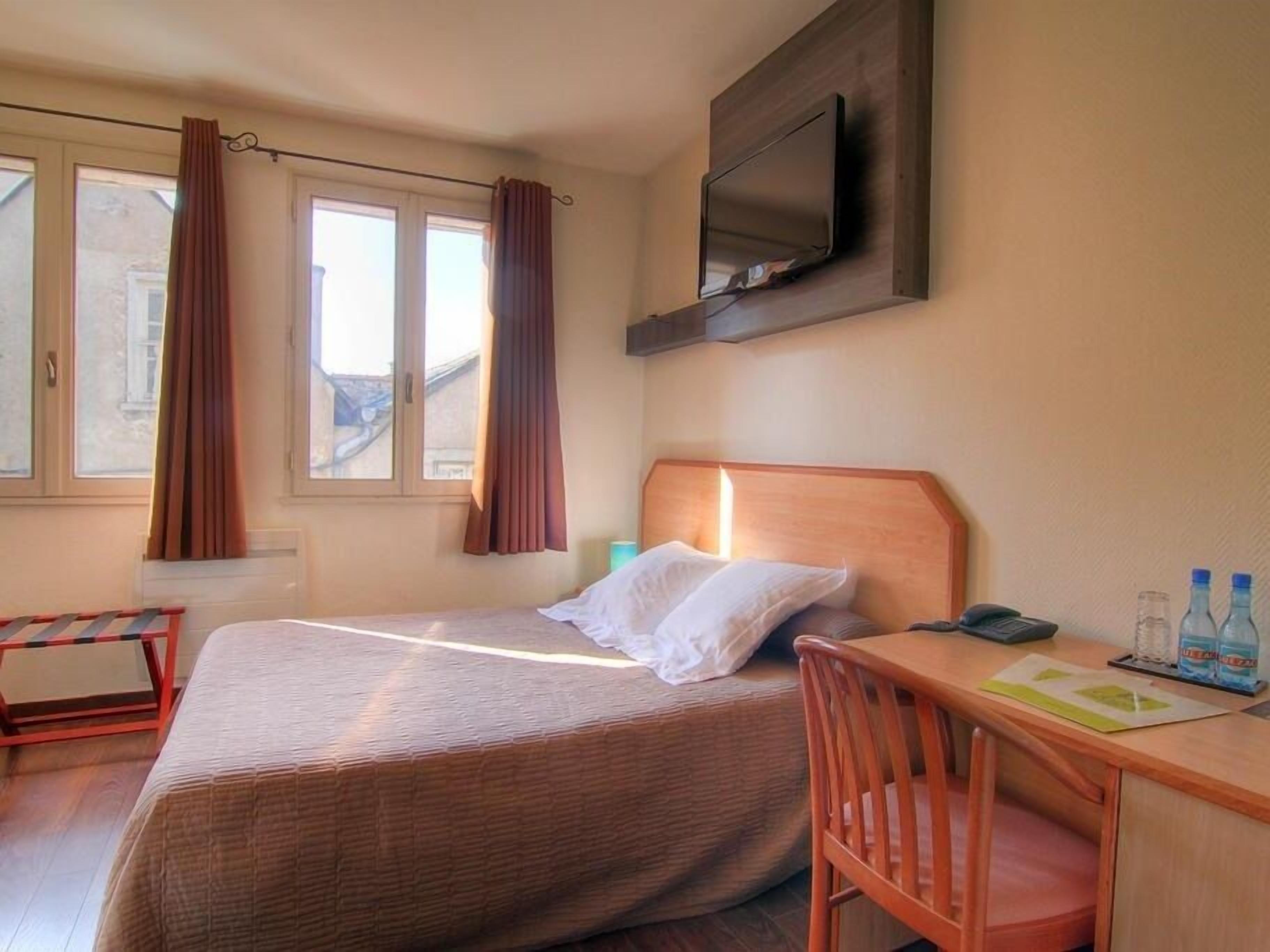 Une chambre d’hôtel équipée d’un lit, d’un bureau, d’une chaise, d’un téléviseur fixé au mur et d’une fenêtre avec des rideaux.