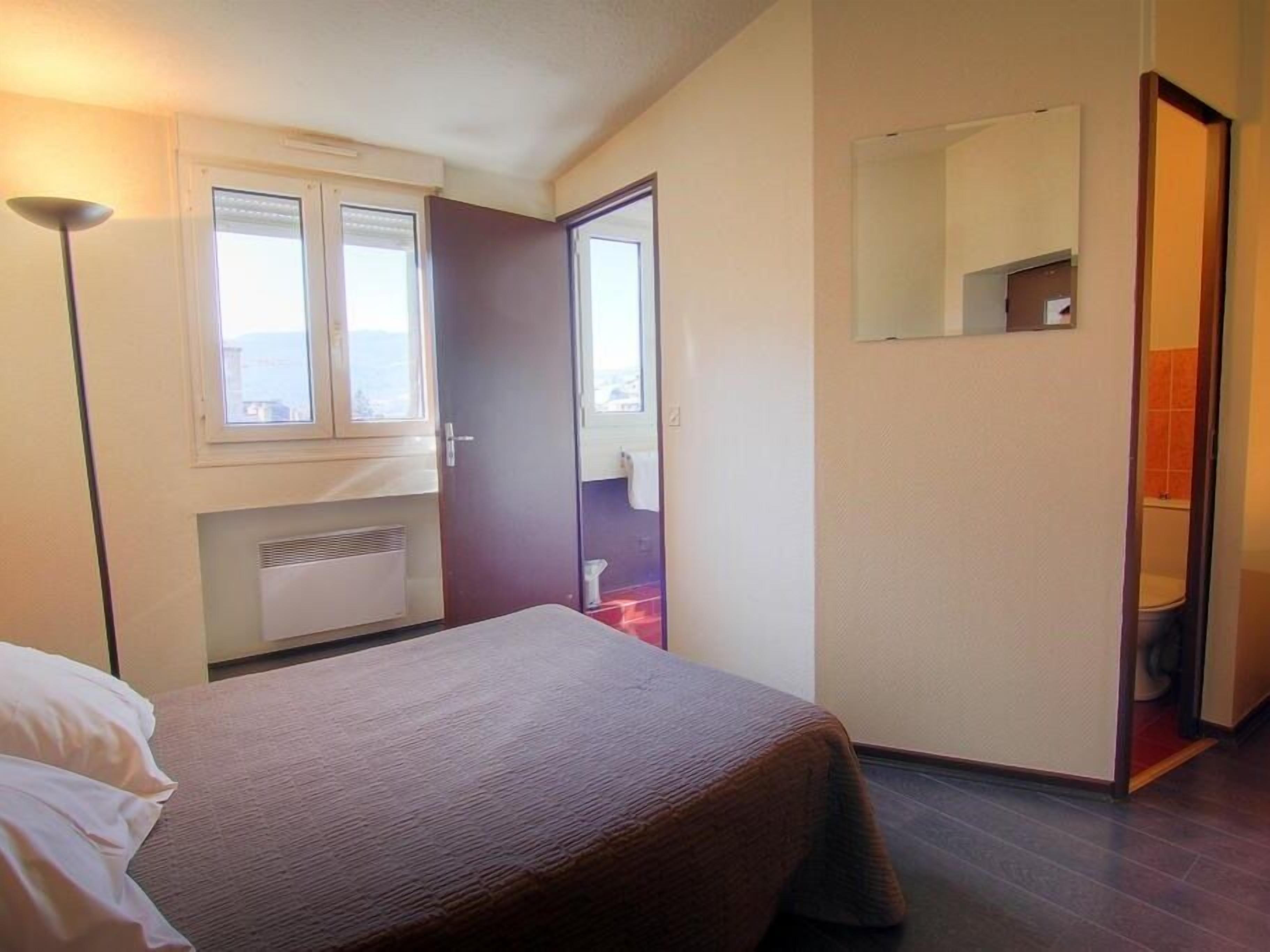 Une chambre à coucher avec un lit, une fenêtre, un radiateur, une porte donnant sur une salle de bain et un miroir au mur.