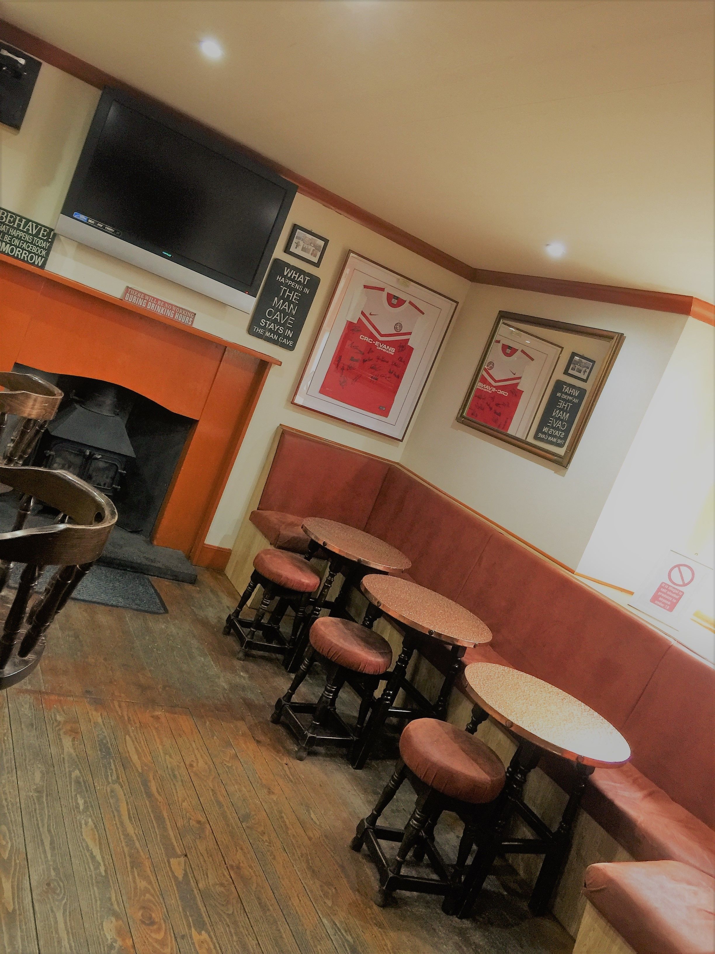 A cozy corner with wooden flooring, a fireplace, and a television mounted on the wall. There are several wooden stools and a bench with cushioned seats.