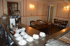 A hotel dining area with a coffee machine, tables, chairs, and a variety of white teapots and cups. - Belgrave Arms Hotel (Helmsdale)