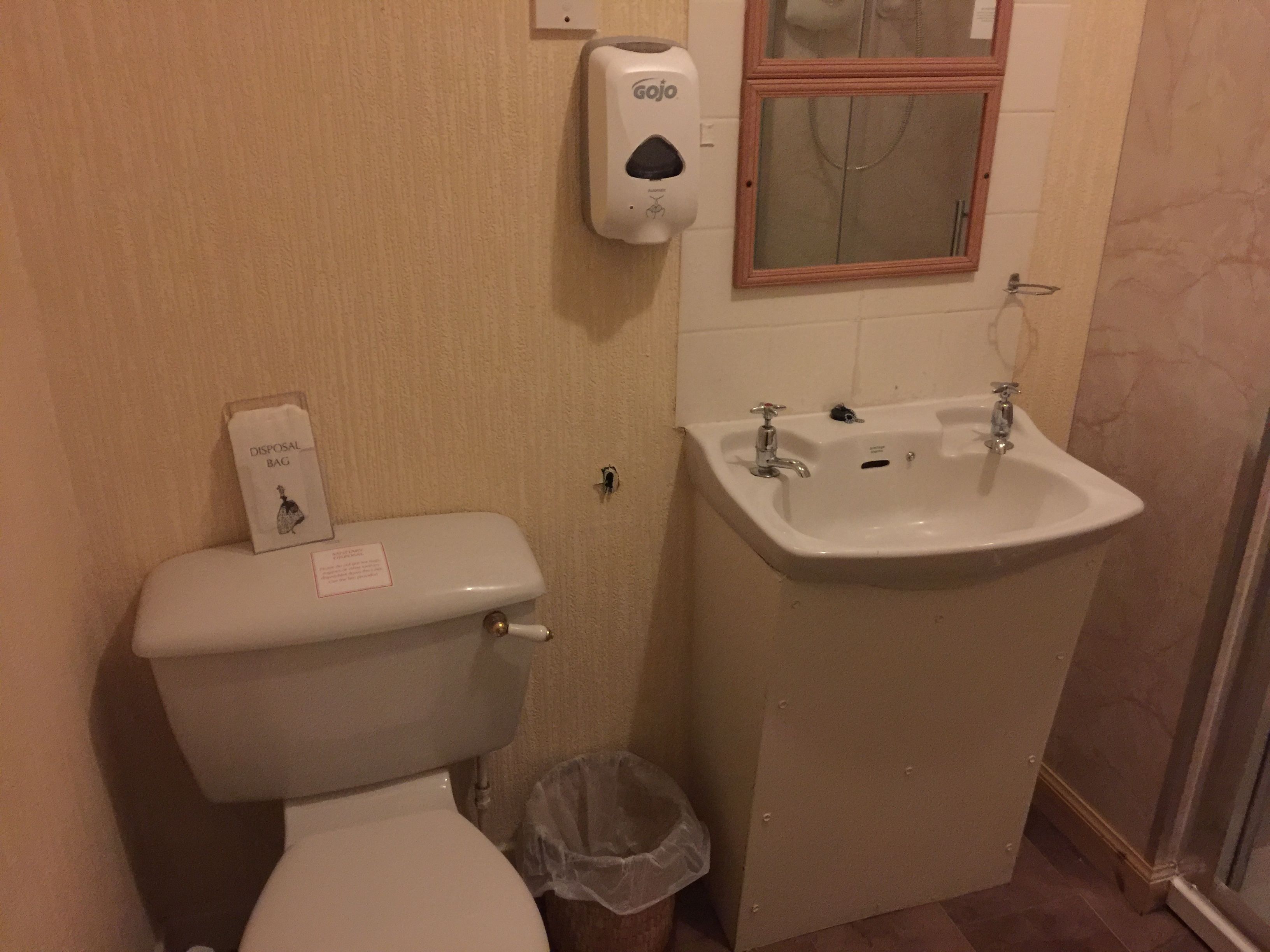 A bathroom with a toilet, a sink, and a hand sanitizer dispenser.