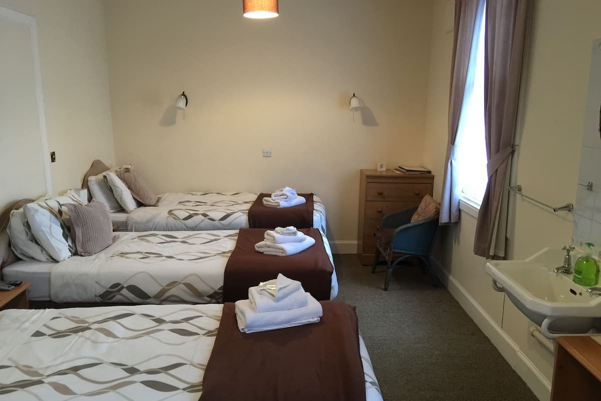 A hotel room with two beds, a desk, a chair, a dresser, and a bathroom with a sink and mirror.