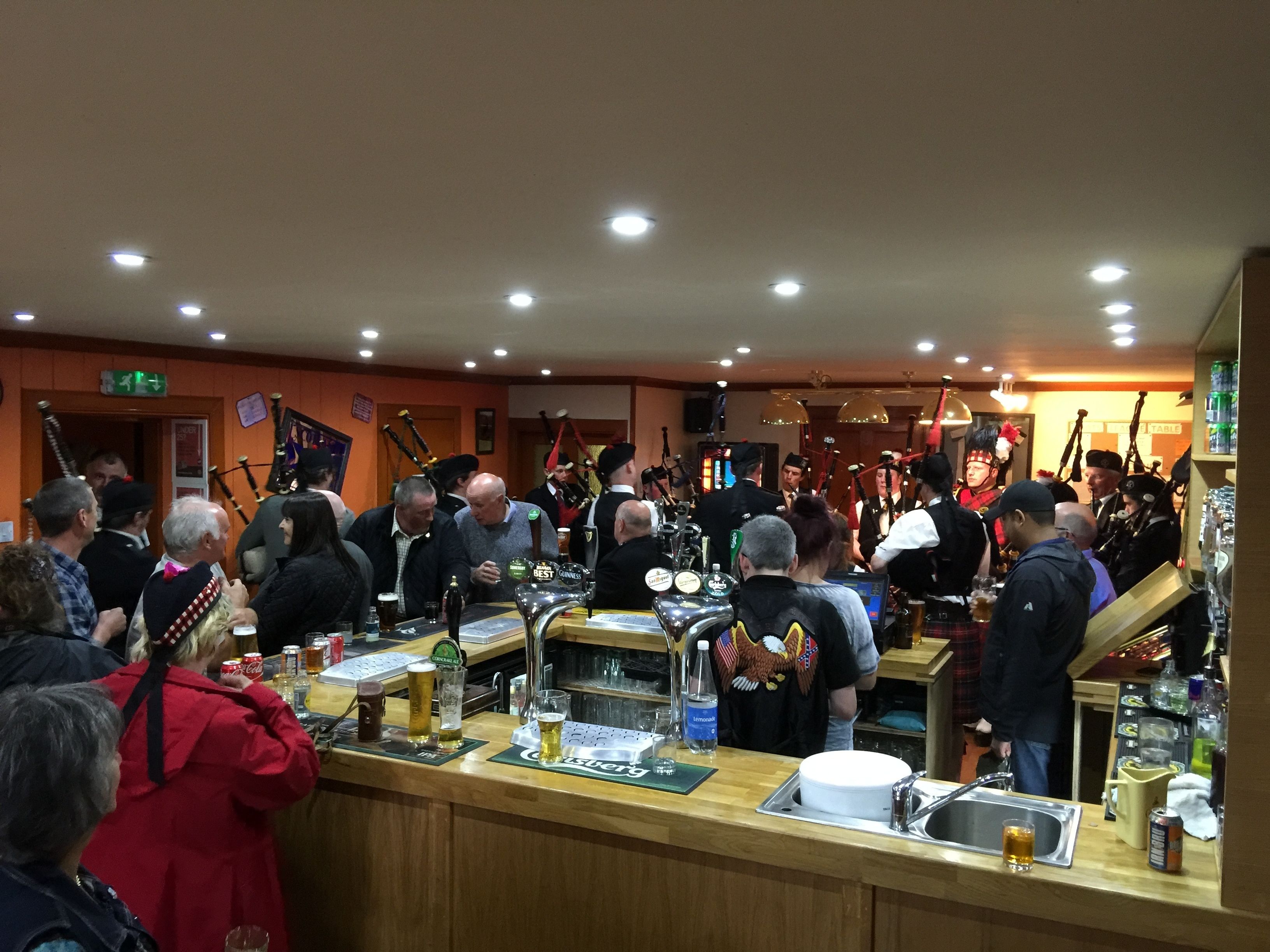 A crowded bar with a counter, stools, and a group of people.