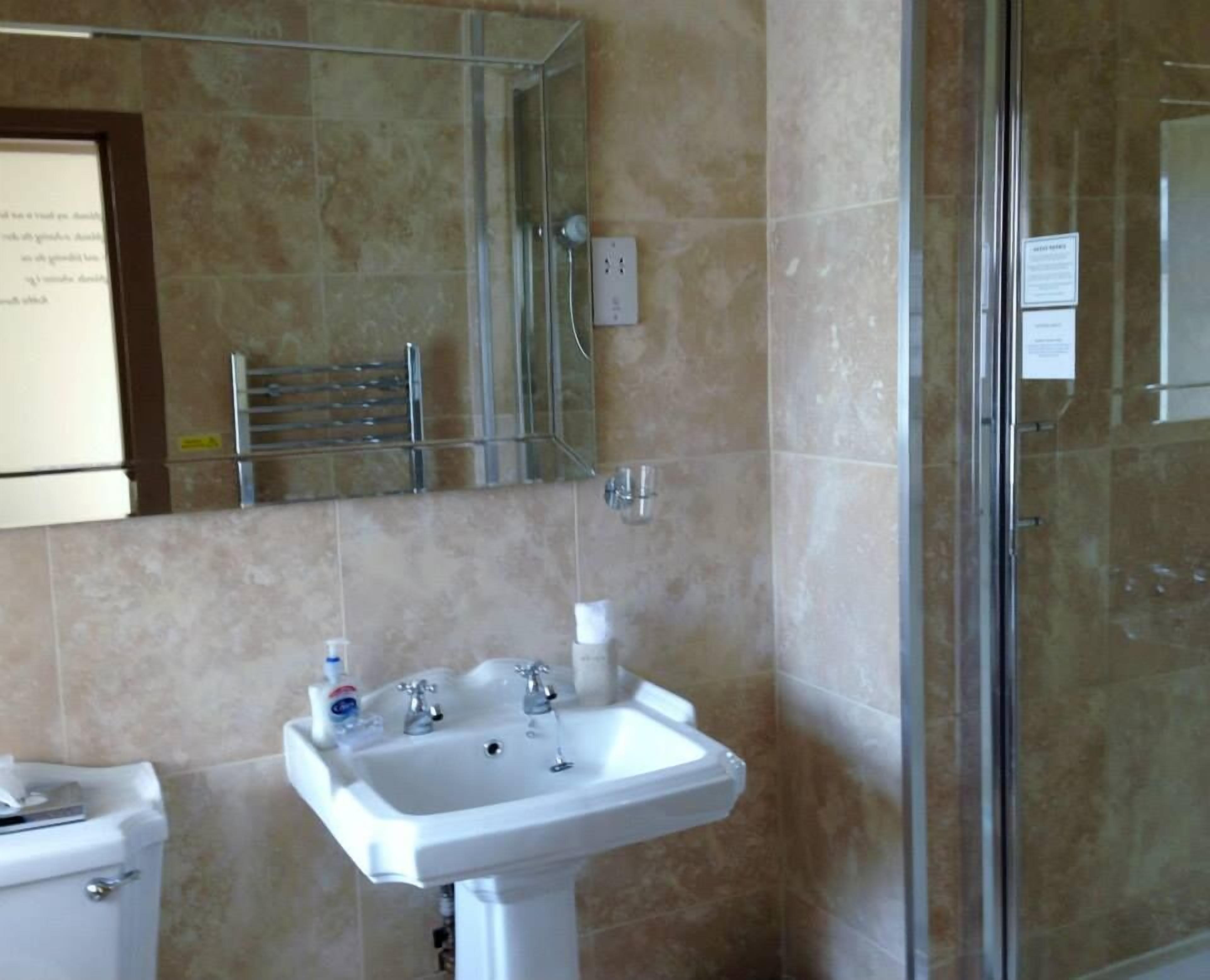 A bathroom with a white sink, a glass shower enclosure, and beige tiles.