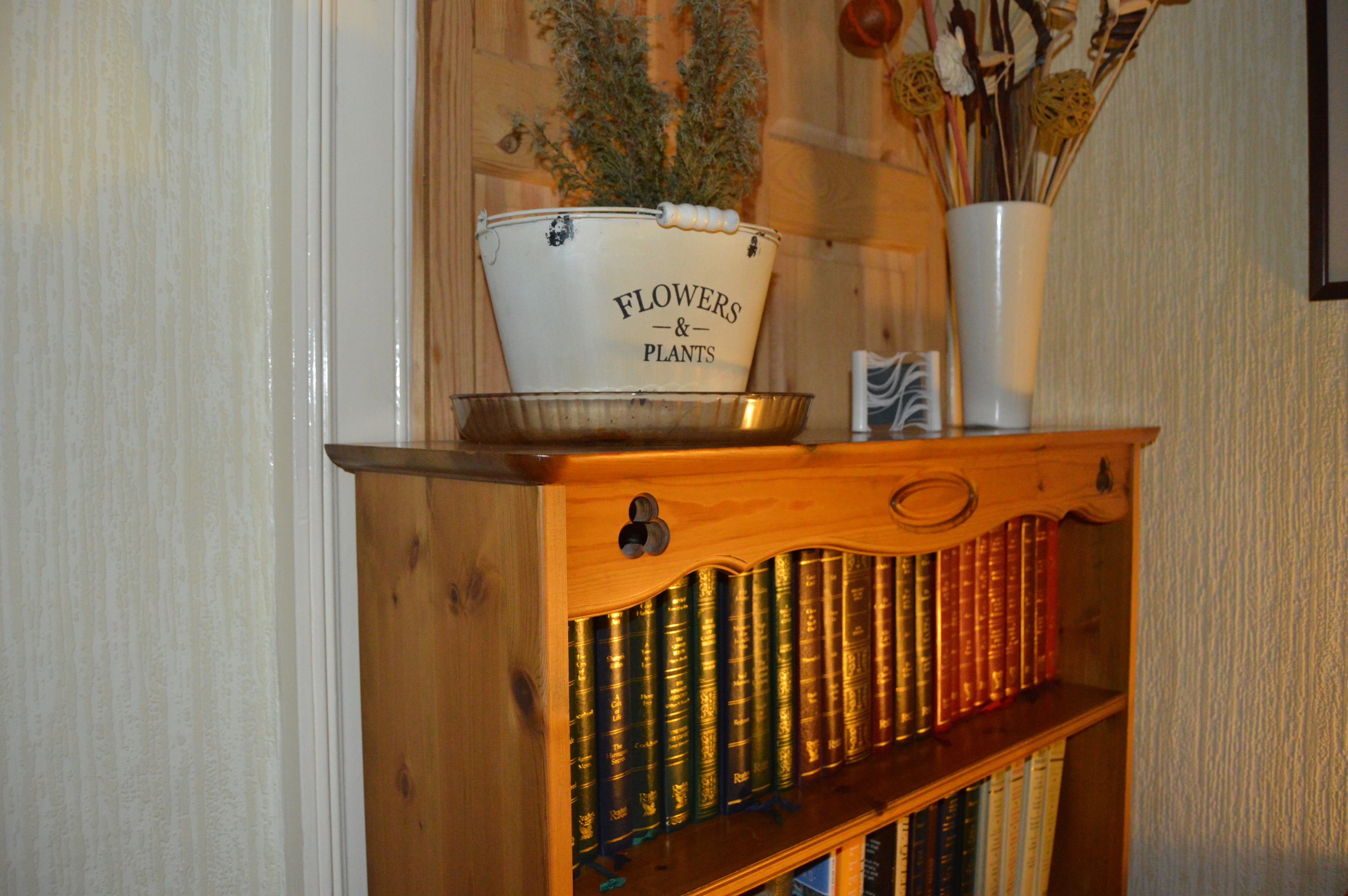 A wooden bookshelf with books and a white pot labeled "Flowers & Plants" on top.