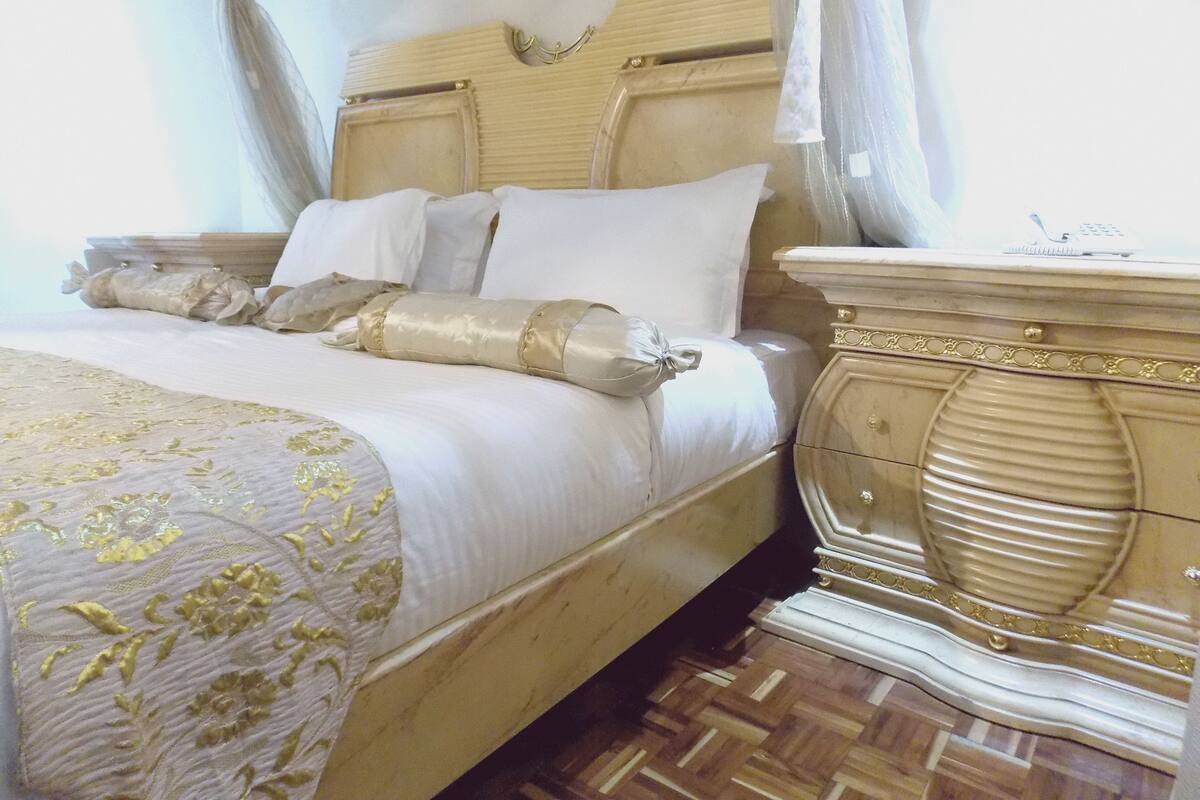 A bed with a canopy, a bedside table with a telephone, and a patterned bedspread.