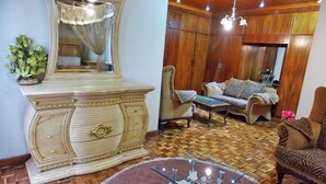 A living room with a wooden floor, a glass coffee table, a beige sofa, and a large mirror with a decorative frame. - Hanan Guest House (Nairobi)